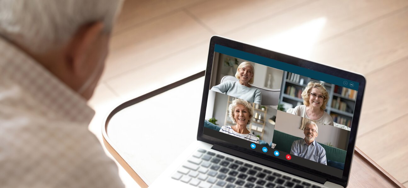 Older generation and modern technologies for virtual visual communication concept. Old man makes videocall talking with relatives or friends by video conference app, pc screen view over male shoulder