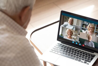 Older generation and modern technologies for virtual visual communication concept. Old man makes videocall talking with relatives or friends by video conference app, pc screen view over male shoulder